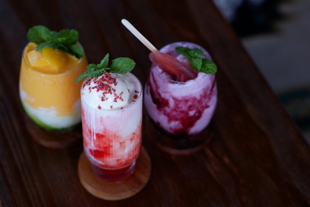 Colorful fruit smoothies with mint leaves on a wooden table, perfect for summer refreshment.